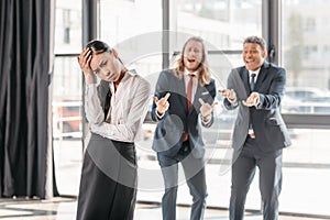 Asian businesswoman standing in office, businessmen behind gesturing and laughing