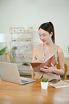 Asian businesswoman taking notes on a notebook, looking at tablet screen