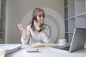 Asian businesswoman talking on mobile phone working on laptop in modern office. Happy business woman talking on mobile