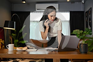 Asian businesswoman talking on the phone with client while looking the details on laptop screen