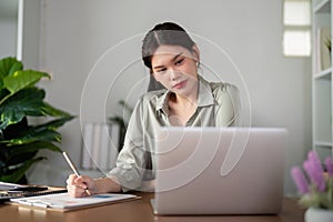 Asian Businesswoman using laptop computer and working at home with calculator document on desk, doing planning analyzing