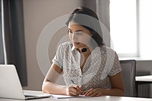 Asian businesswoman wear headset watching webinar make call write notes