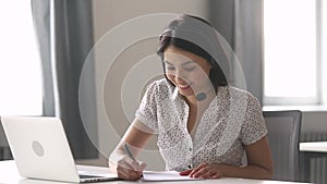 Asian businesswoman wearing headset make notes talk by conference call