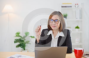 Asian businesswoman wearing suit and glasses holding magnifying glass and working laptop. Seaching browsing. Entrepreneur woman or