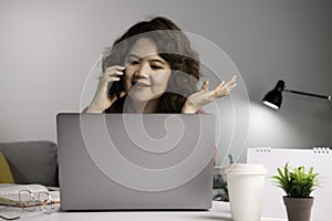 Asian businesswoman work at home with laptop and talking on smartphone and smiling. Female working on computer and using cell mobi