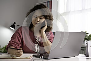 Asian businesswoman work at home with laptop and talking on smartphone and smiling. Female working on computer and using cell mobi