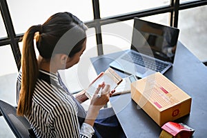 Asian businesswoman working at her desk in her home office, listing her online orders. top view