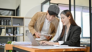 Asian businesswoman working on her tasks on a laptop while being trained by her male boss