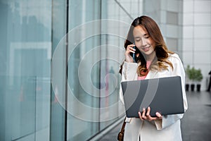 Asian businesswoman working on laptop and talking on cell phone at front