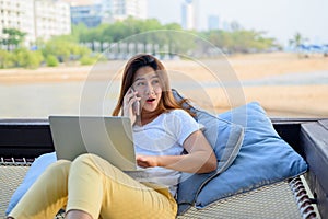 Asian businesswoman working online at the beach. Freelancer using technology for work everywhere. Woman talking with customer