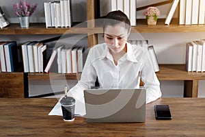 Asian businesswoman is working or online shopping with laptop and drinking hot coffee in workspace at office. Collegian woman are