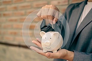 Asian businesswomen hold piggy banks and put coins in piggy banks to save money with coins to step into business, grow successful