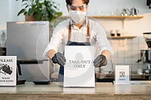 Asian cafe business owner put TAKE OUT ONLY sign on coffee bar counter due to Covid-19 pandemic. Waiter wear face mask and shield,