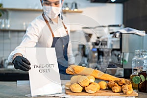 Asian cafe business owner put TAKE OUT ONLY sign on coffee bar counter due to Covid-19 pandemic. Waiter wear face mask and shield,