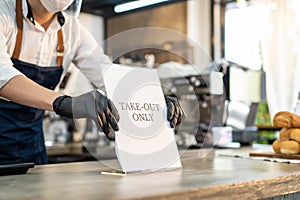 Asian cafe business owner put TAKE OUT ONLY sign on coffee bar counter due to Covid-19 pandemic. Waiter wear face mask and shield