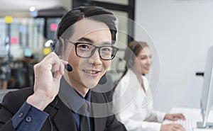 Asian call center agent team, customer service support wearing headset or headphone talking with customer in modern office