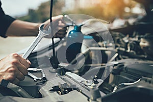 Asian car mechanic holds a wrench and a bottle of lure oil, ready to repair the car