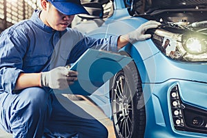 Asian car mechanic technician holding clipboard and checking to maintenance vehicle by customer claim order in auto repair shop