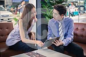 Asian car salesman giving a sale promotions to attractive asian millenials girl at car dealership office