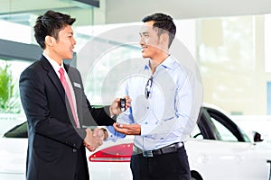 Asian Car Salesman selling auto to customer