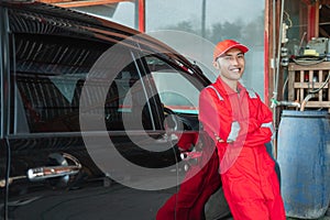 Asian car washer in red uniform standing smiling leaning against the car