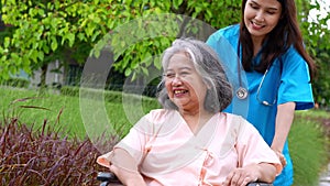 Asian careful caregiver or nurse taking care of the patient in a wheelchair.  Concept of happy retirement with care from a