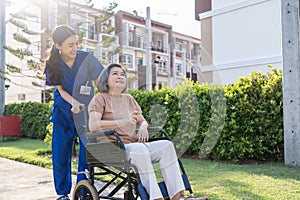 Asian caregiver nurse support old disabled woman on wheelchair outdoor. Beautiful girl doctor help and take care of senior elder