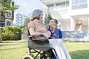 Asian caregiver nurse support old disabled woman on wheelchair outdoor. Beautiful girl doctor help and take care of senior elder