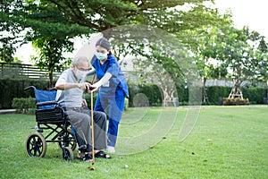 Asian Caregiver wear mask, take care senior disabled man on wheelchair. Young beautiful woman carer nurse at nursing home support