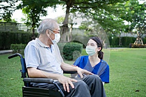 Asian Caregiver wear mask, take care senior disabled man on wheelchair. Young beautiful woman carer nurse at nursing home talk and