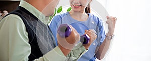 Asian caregiver woman or nurse training senior man lifting dumbbell for arm exercise.