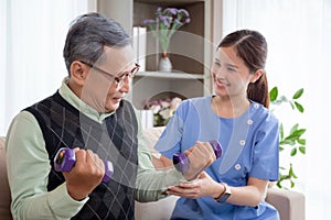 Asian caregiver woman or nurse training senior man lifting dumbbell for arm exercise while therapy.