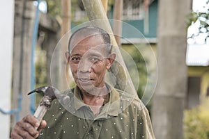 An asian carpenter holding a hammer. Wearing an old faded collared shirt. Rural livelihood concept photo