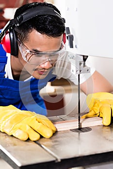 Asian carpenter or worker on saw with wood