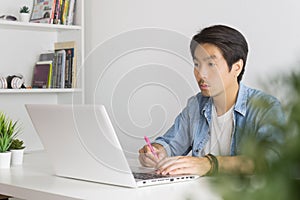 Asian Casual Businessman or Freelancer Working with Laptop and Note Detail in Home Office