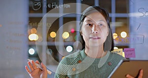 Asian casual businesswoman using tablet presenting to colleagues at night in office