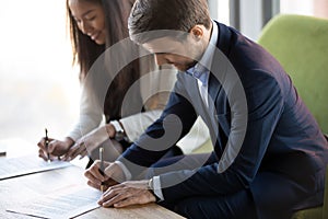 Asian and caucasian businesspeople sitting at desk signing contr