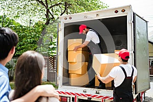 Asian and Caucasian workers in uniform unloading cardboard boxes from the truck. Delivery men unloading boxes and check.