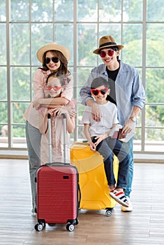 Asian cheerful happy family mom dad son and daughter wearing sunglasses and hat standing posing with two trolley luggages smiling