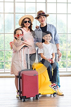 Asian cheerful happy family mom dad son and daughter wearing sunglasses and hat standing posing with two trolley luggages smiling