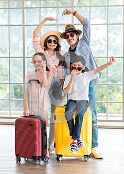 Asian cheerful happy family mom dad son and daughter wearing sunglasses and hat standing posing with two trolley luggages smiling