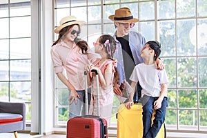 Asian cheerful happy family mom dad son and daughter wearing sunglasses and hat standing posing with two trolley luggages smiling