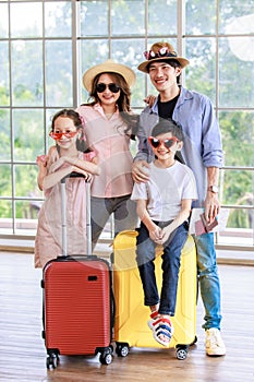 Asian cheerful happy family mom dad son and daughter wearing sunglasses and hat standing posing with two trolley luggages smiling