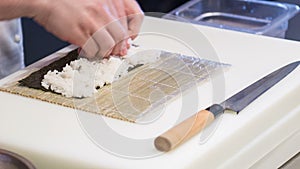 Asian chef in white uniform preparing sushi rolls