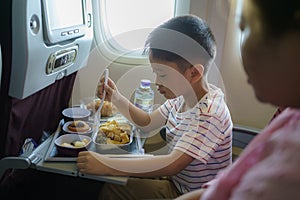 Asian Child in airplane window seat. Kids flight meal. Children fly. Special inflight menu, food and drink for baby and kid. Boy