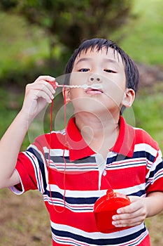 Asian child blowing soap bubbles in summer park, nature backgrou