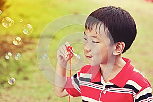 Asian child blowing soap bubbles in summer park, nature background