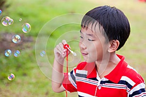 Asian child blowing soap bubbles in summer park, nature background