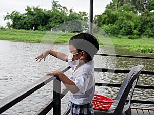 Asian child boy feeding bread to fish at pond. Asian family travel outdoor together.