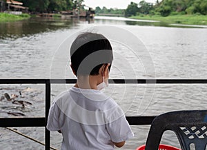 Asian child boy feeding bread to fish at pond. Asian family travel outdoor together.